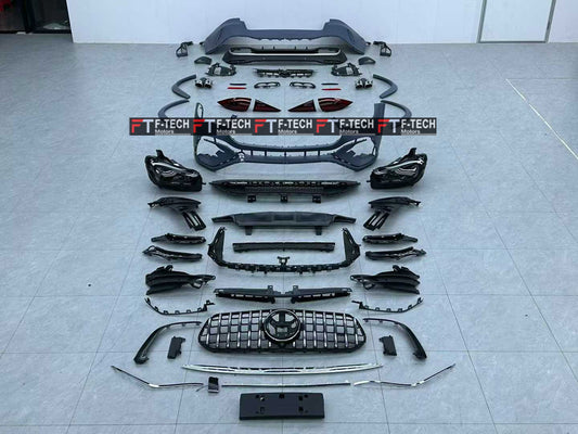A full set of black car body parts and trim accessories laid out in a row on a light gray tiled floor. The kit includes a front bumper, grille, headlights, fog light housings, side skirts, trim pieces, and other automotive body components.