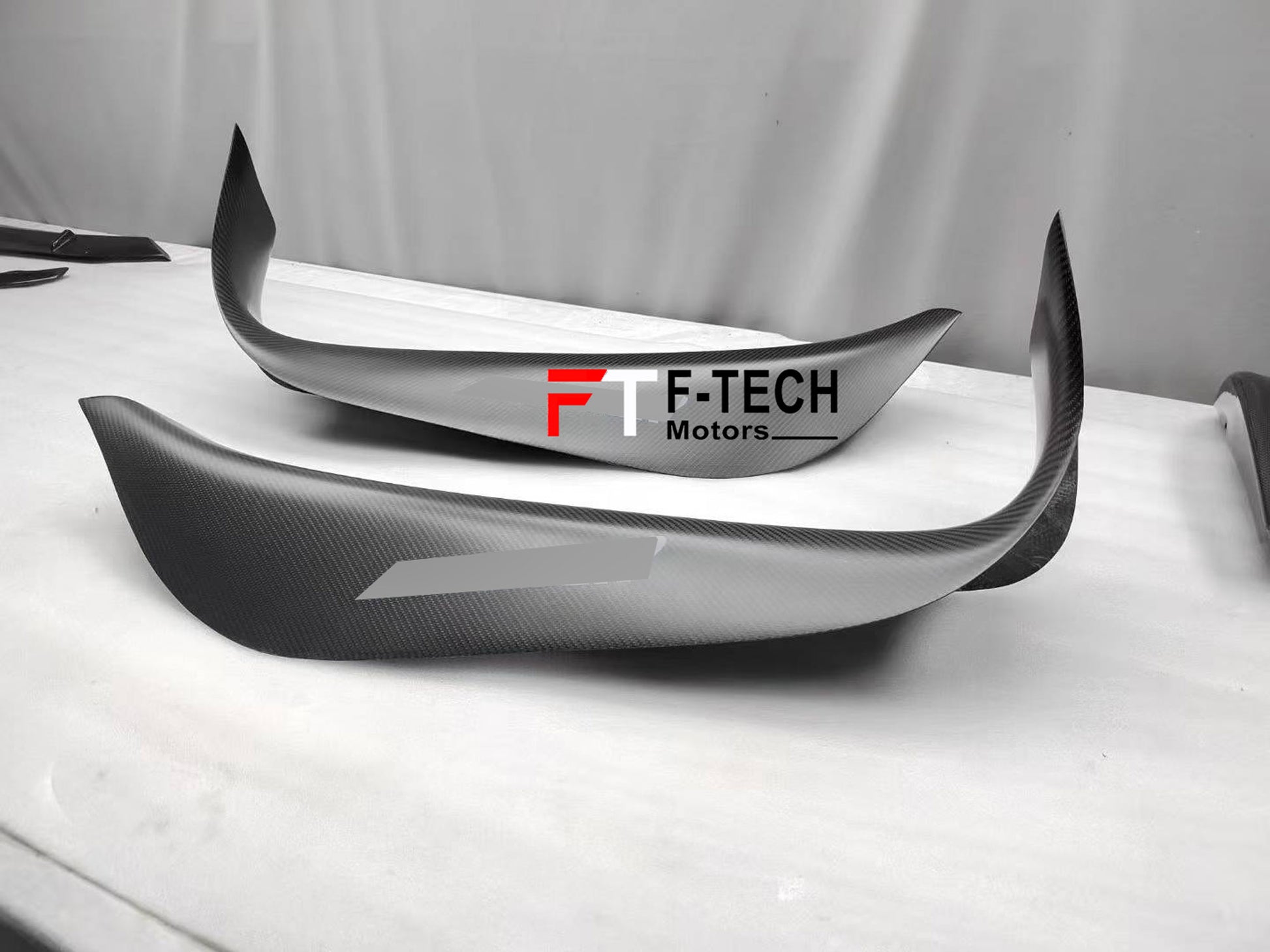 Carbon fiber car bumper with F-Tech Motors branding on a white surface.