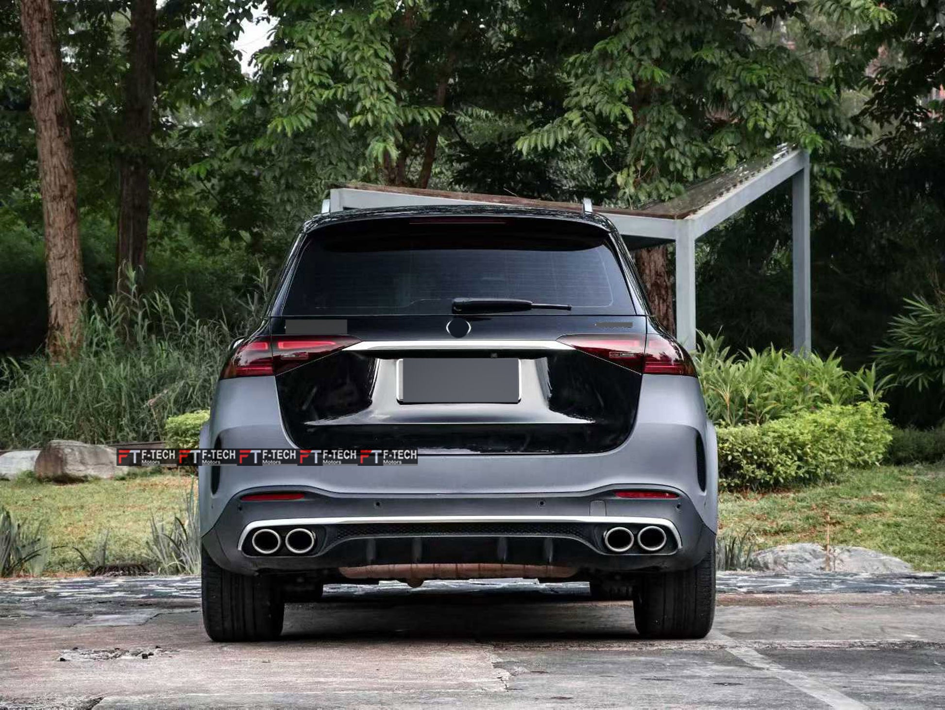 Rear view of a dark gray Mercedes-Benz SUV parked outdoors on a paved surface with trees and greenery in the background.