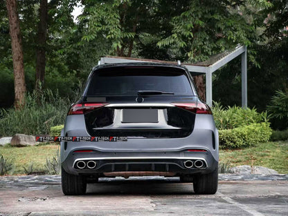 Rear view of a dark gray Mercedes-Benz SUV parked outdoors on a paved surface with trees and greenery in the background.