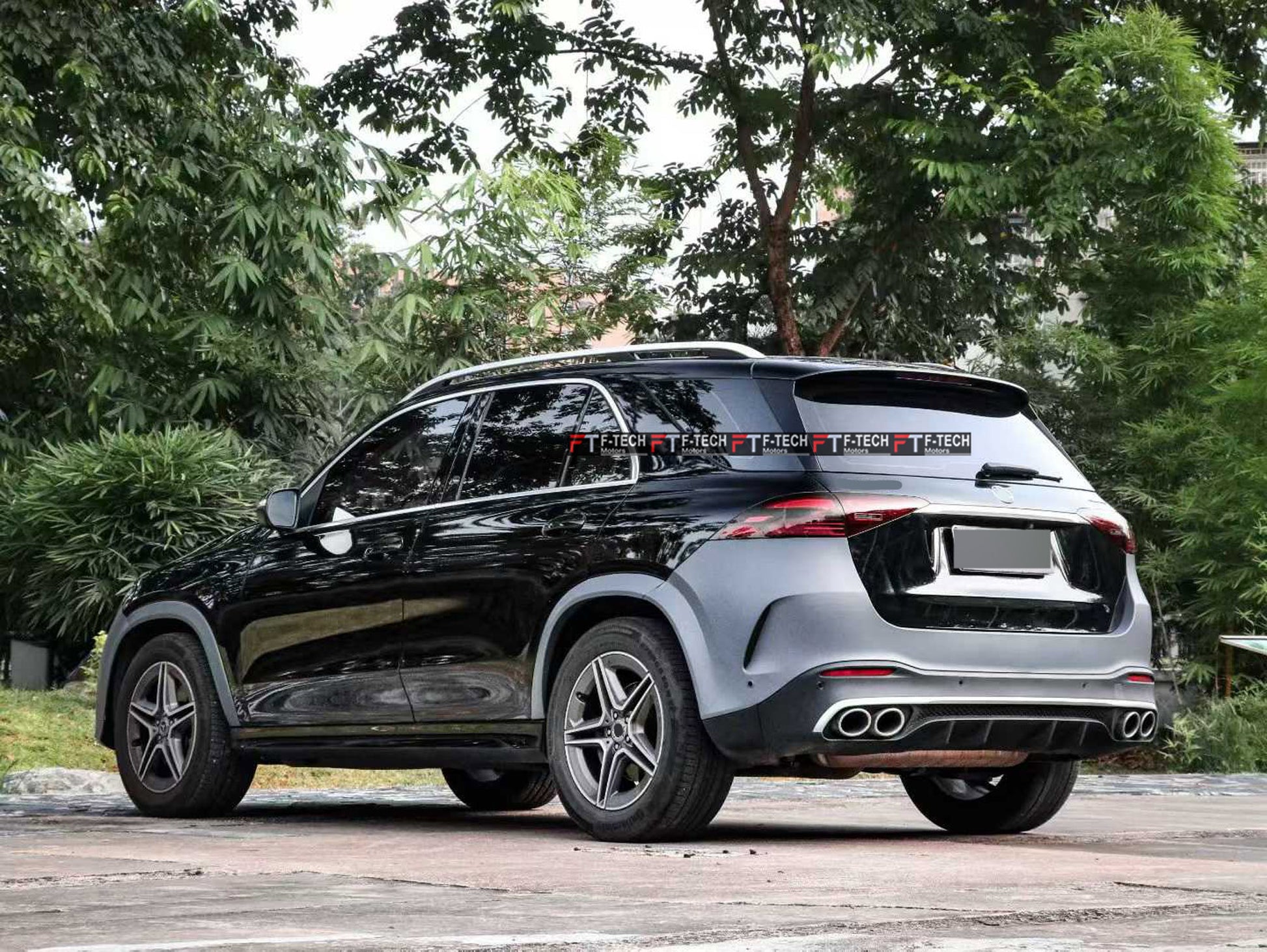 A black Mercedes-Benz GLA SUV shown from a rear three-quarter angle, parked outdoors on a paved surface with green trees in the background. The vehicle features a distinctive dark gray rear panel and a black rear spoiler.