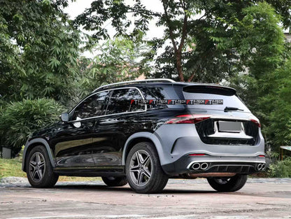 A black Mercedes-Benz GLA SUV shown from a rear three-quarter angle, parked outdoors on a paved surface with green trees in the background. The vehicle features a distinctive dark gray rear panel and a black rear spoiler.